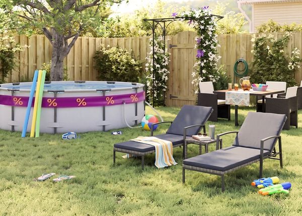Sonniger Garten hinter dem Haus mit Aufstellpool, Poolnudeln, Schwimmbrille, Wasserball und Flip-Flops im Gras. Zwei schwarze Metall-Sonnenliegen mit grauen Auflagen stehen neben einem kleinen Beistelltisch, w&auml;hrend eine Outdoor-Essgruppe mit dunklen Geflechtsesseln bei einer bl&uuml;henden Pergola, einem Holzzaun und sommerlichen Gartenaccessoires platziert ist.