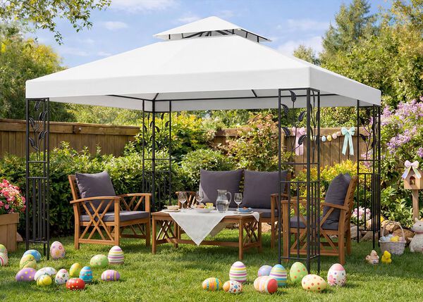 Gartenm&ouml;bel-Set unter einem wei&szlig;en Pavillon mit Holzst&uuml;hlen und Tisch f&uuml;r ein Osterfest arrangiert, bunte Ostereier auf gr&uuml;nem Rasen, bl&uuml;hende Blumen und Fr&uuml;hlingsdekoration im sonnigen Garten.