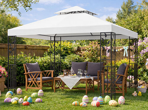 Gartenm&ouml;bel-Set unter einem wei&szlig;en Pavillon mit Holzst&uuml;hlen und Tisch f&uuml;r ein Osterfest arrangiert, bunte Ostereier auf gr&uuml;nem Rasen, bl&uuml;hende Blumen und Fr&uuml;hlingsdekoration im sonnigen Garten.