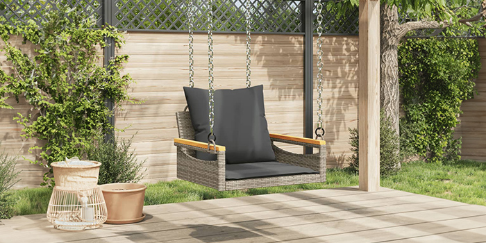 Rattan-Schaukelbank für draussen mit dunklen Kissen auf einer Terrasse. Klick drauf, um die Kollektion zu shoppen.